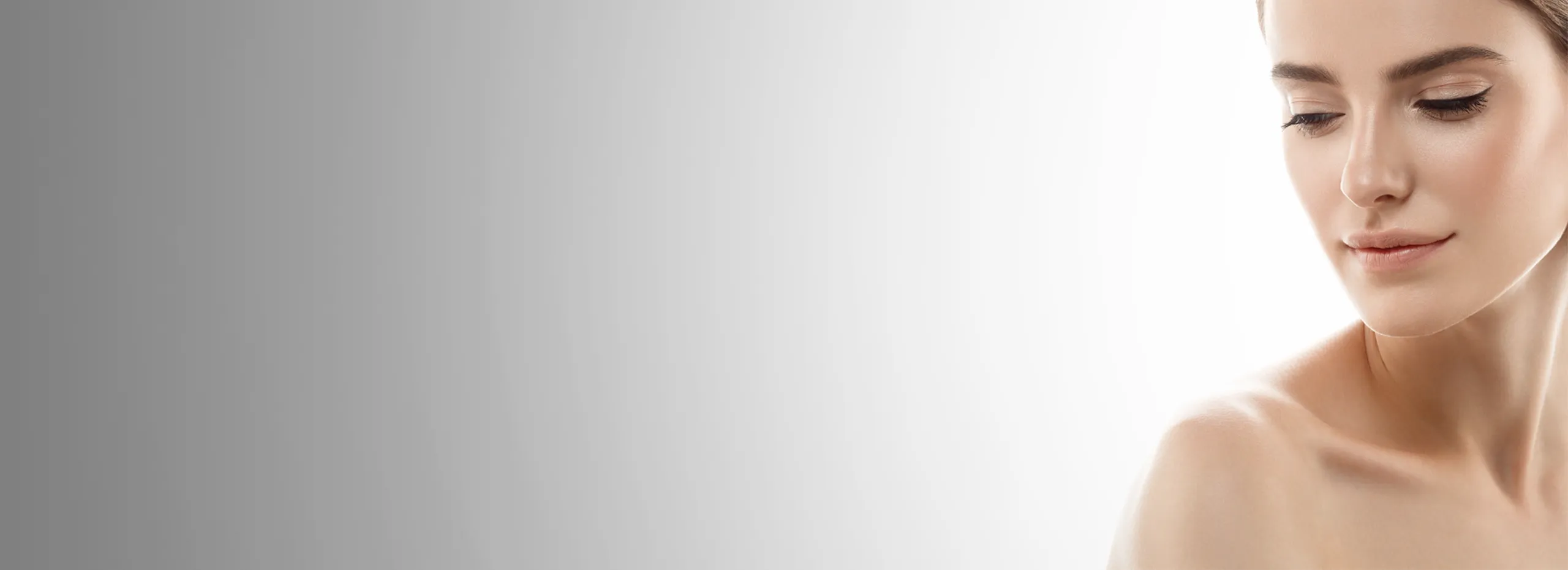 Das Bild zeigt den seitlichen Teil eines Gesichts einer Frau vor einem sanften Farbverlauf von grau zu weiß. Sie hat die Augen geschlossen und ein leichtes Lächeln. Der Fokus liegt auf ihrem Gesicht.