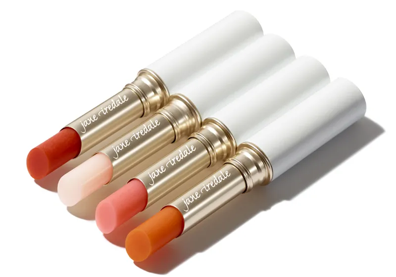 Vier Lippenstifte in Goldhülsen mit weißem Deckel liegen nebeneinander auf weißem Hintergrund. Die Farben sind von links nach rechts rot, beige, rosa und orange. Auf den Hülsen steht "jane iredale".