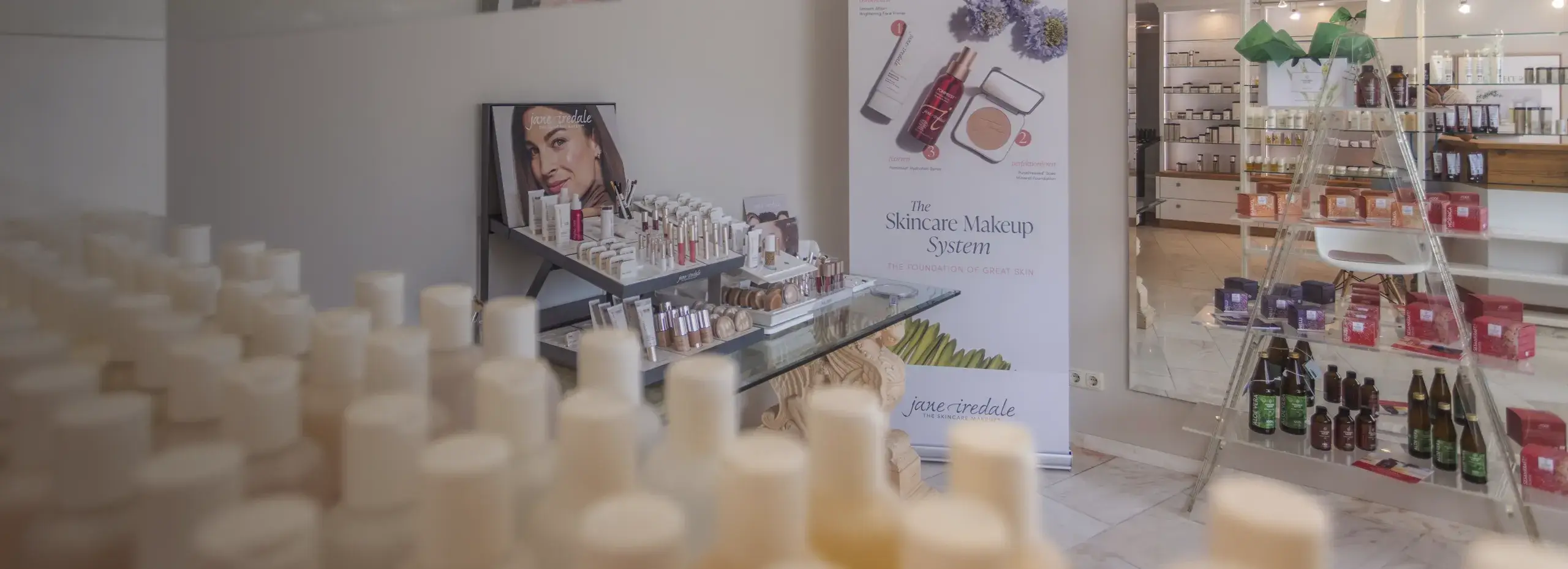 Ein Kosmetikgeschäft mit Regalen voller verschiedener Kosmetikprodukte. Es gibt Poster mit Produktabbildungen und ein Fotoporträt einer Person. Die Atmosphäre ist hell und sauber.