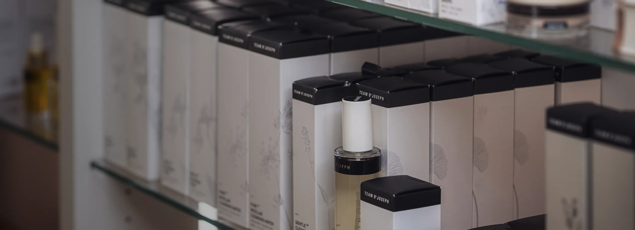 Regale mit kosmetischen Produkten in rechteckigen Verpackungen. Einige Boxen sind geöffnet und zeigen Flaschen mit Pumpspendern. Die Farben der Verpackungen sind überwiegend hell mit dunklen Verschlüssen.